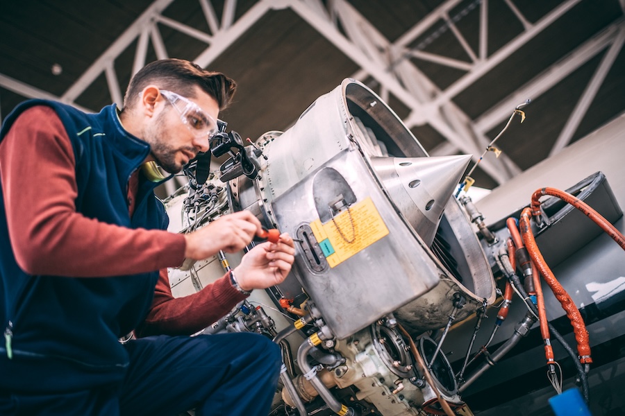 Aircraft engineer in the hangar repairing and maintaining airplane jet engine.