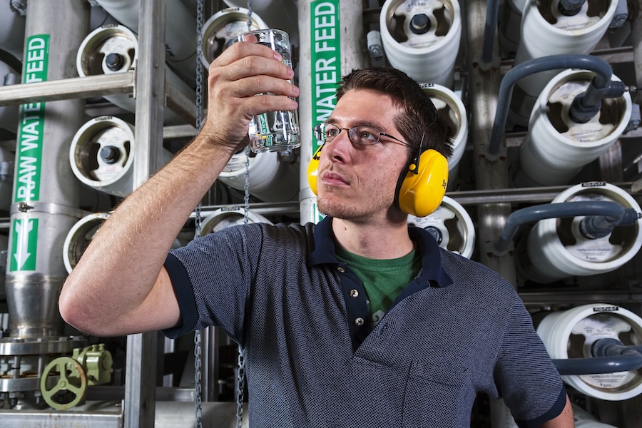 A water technician exams a glass of water after tapping one of the filters behind him at a public water facility.